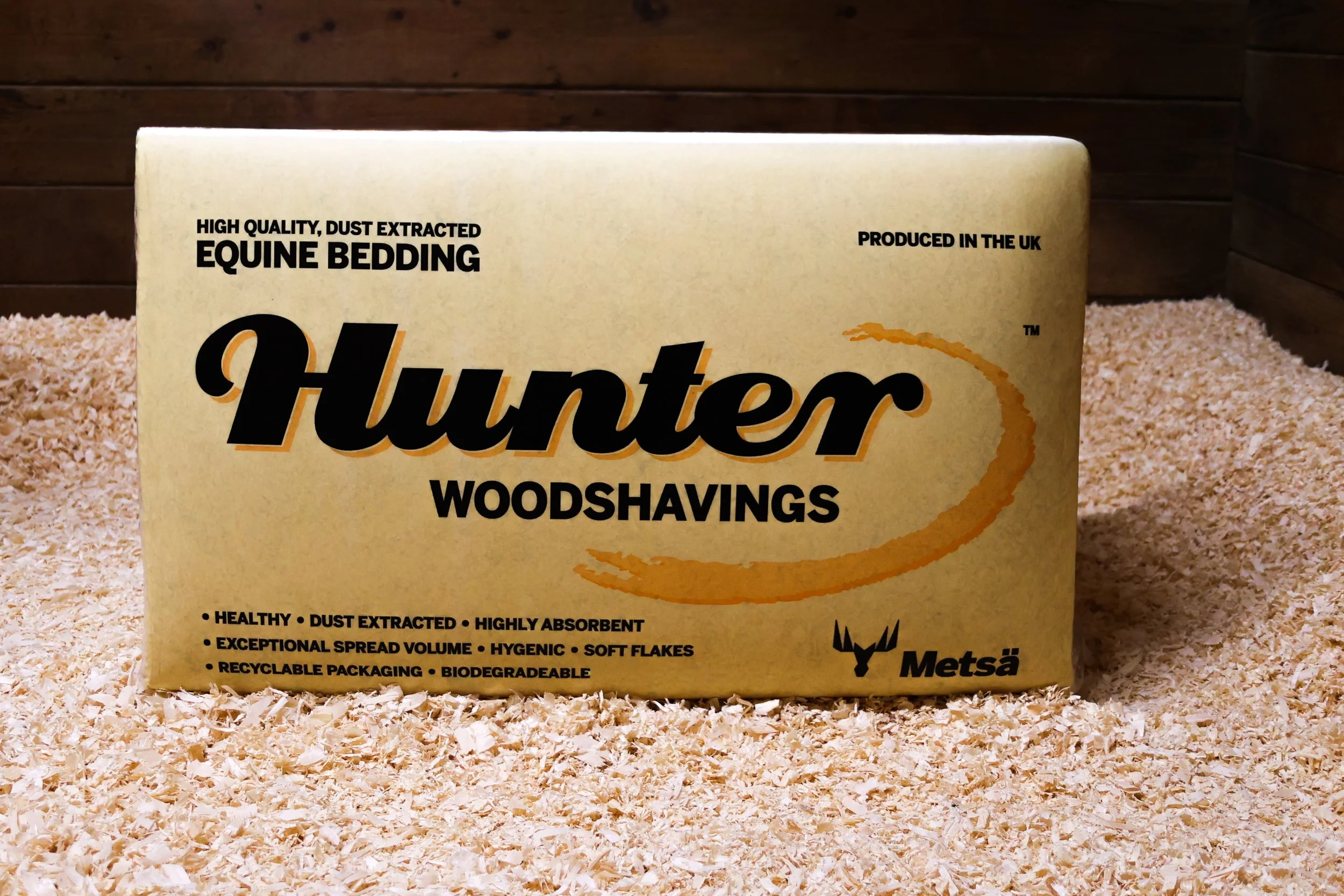A yellow box of Hunter equine bedding on a bedding of wood shavings with wooden walls in the background.