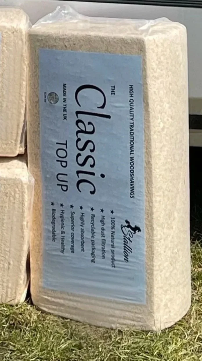 A block of traditional wood shavings labeled as 'The Classic Top Up' from the UK, made of 100% natural product, high-quality, biodegradable, and used for bedding and hygiene.
