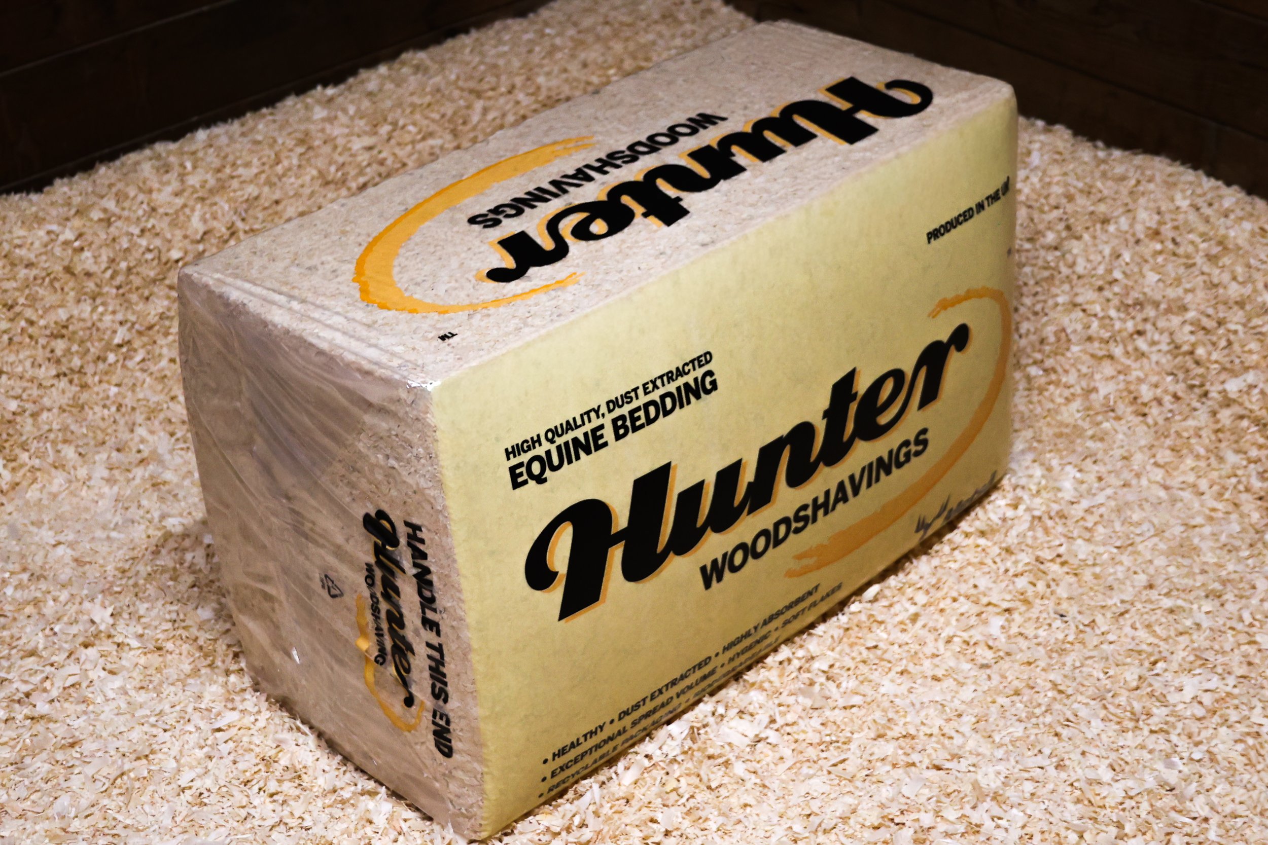 A block of shavings on a countertop with part of a yellow and black bag of bedding for horses, labeled "Shavings" and mentioning high quality, dust extracted, and wood shavings.