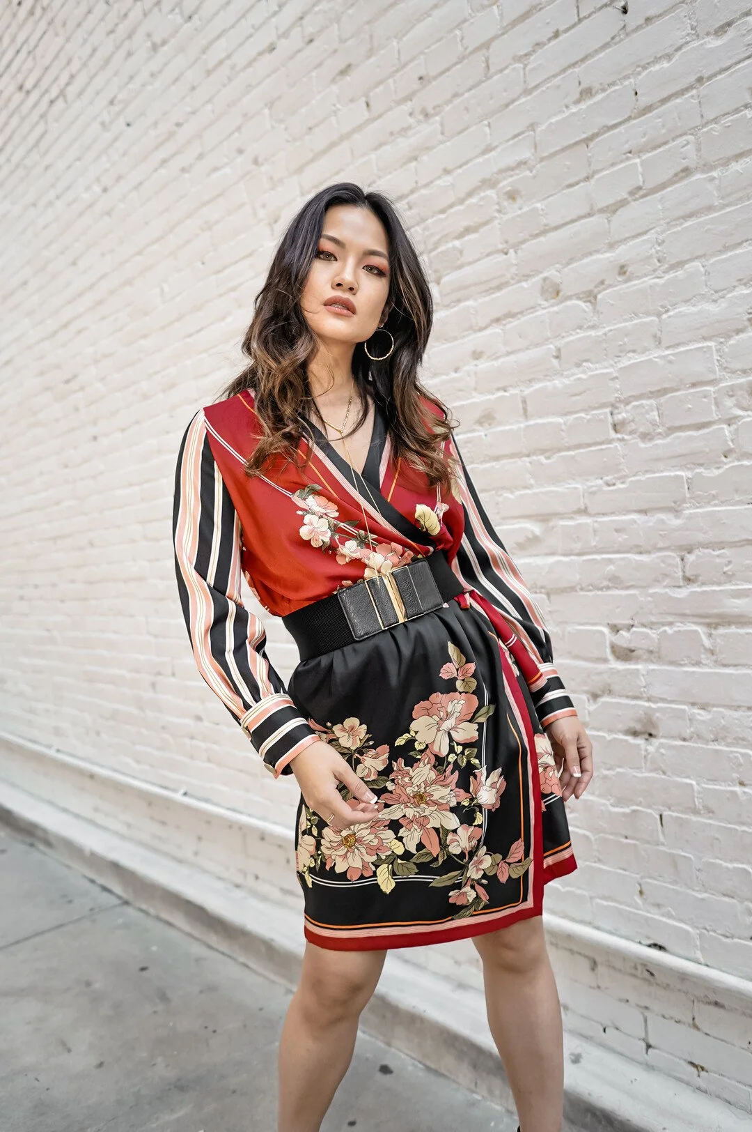 Woman in patterned dress standing against a brick wall