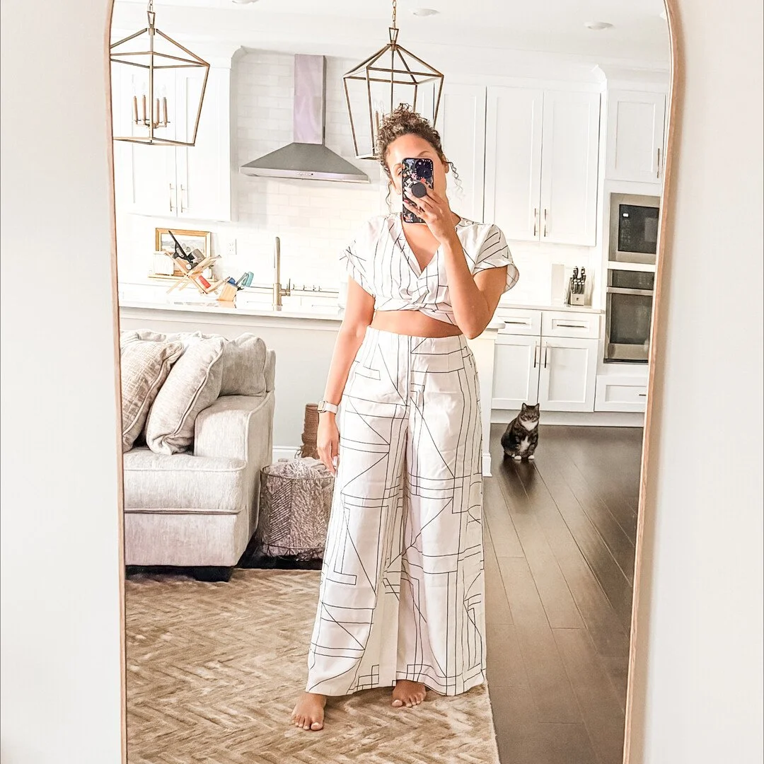 Woman taking a mirror selfie in a modern kitchen, wearing a geometric pattern set, with a cat sitting on the floor.
