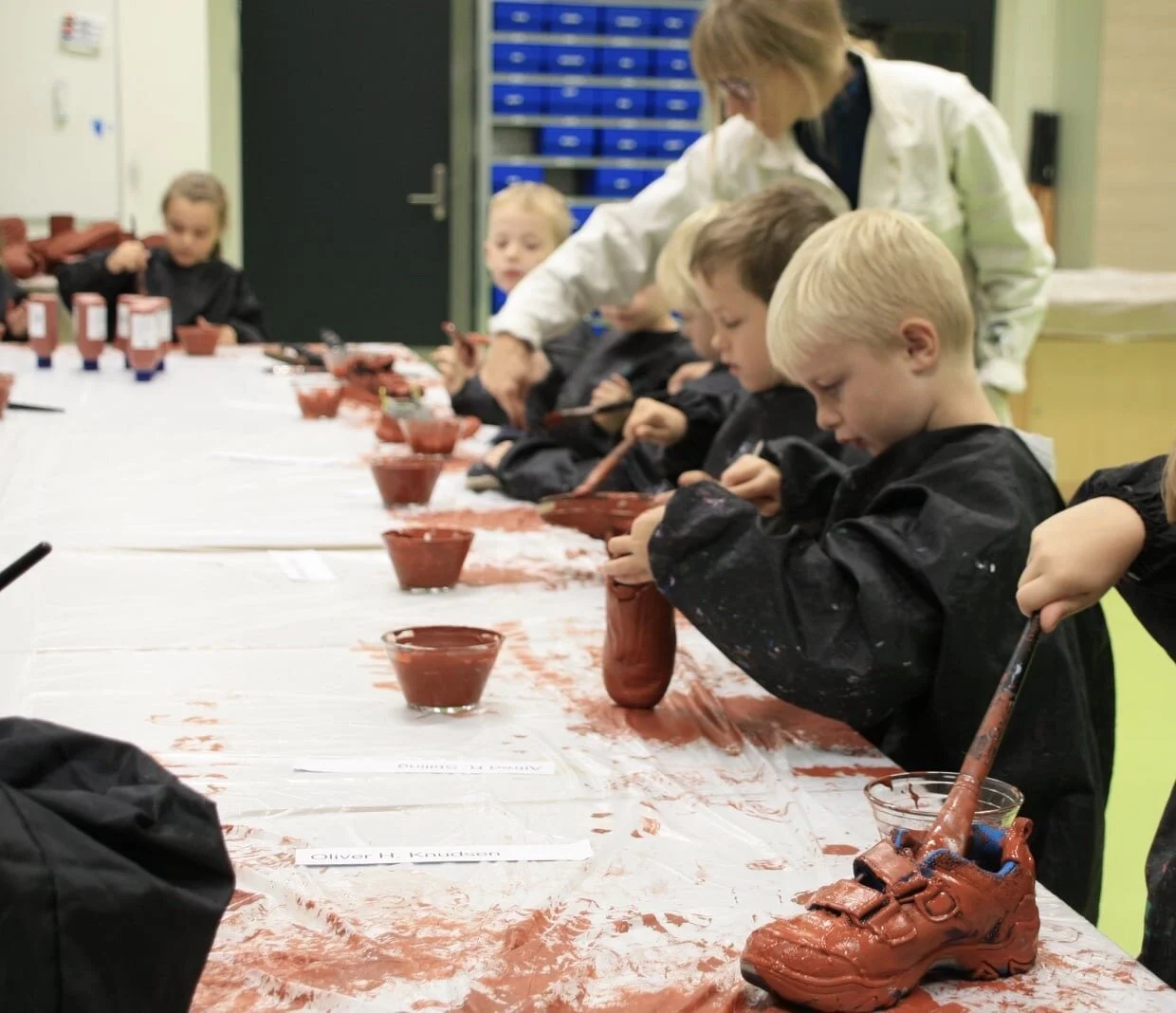 Skotræet, Vestbyen Friskole, Holstebro, 2020.
Elever maler deres aflagte sko på værkstedet - i skolens rustrøde nuance.