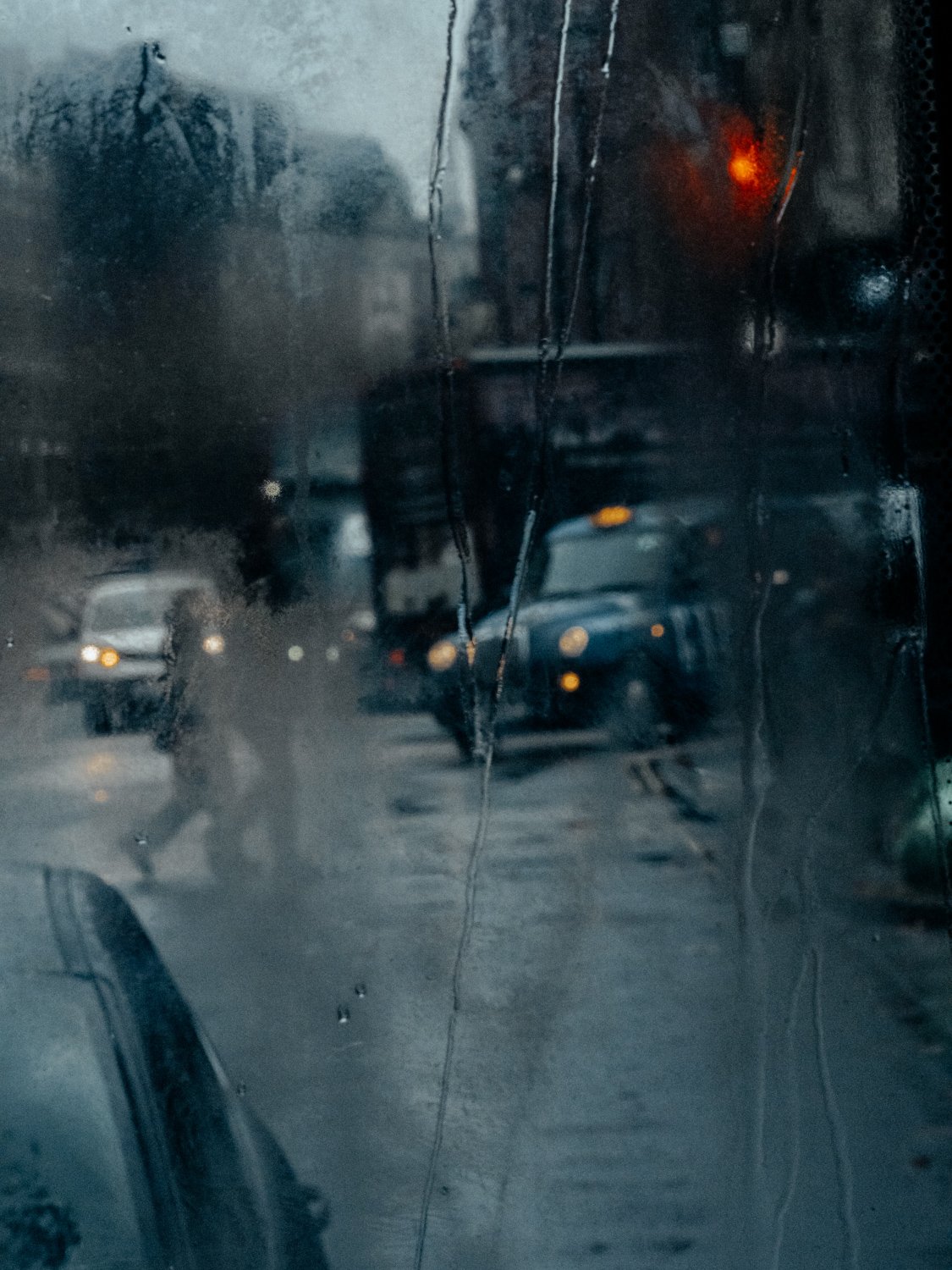 Black cab and pedestrians seen through a rain-streaked bus window, London street photography by Joshua K. Jackson.