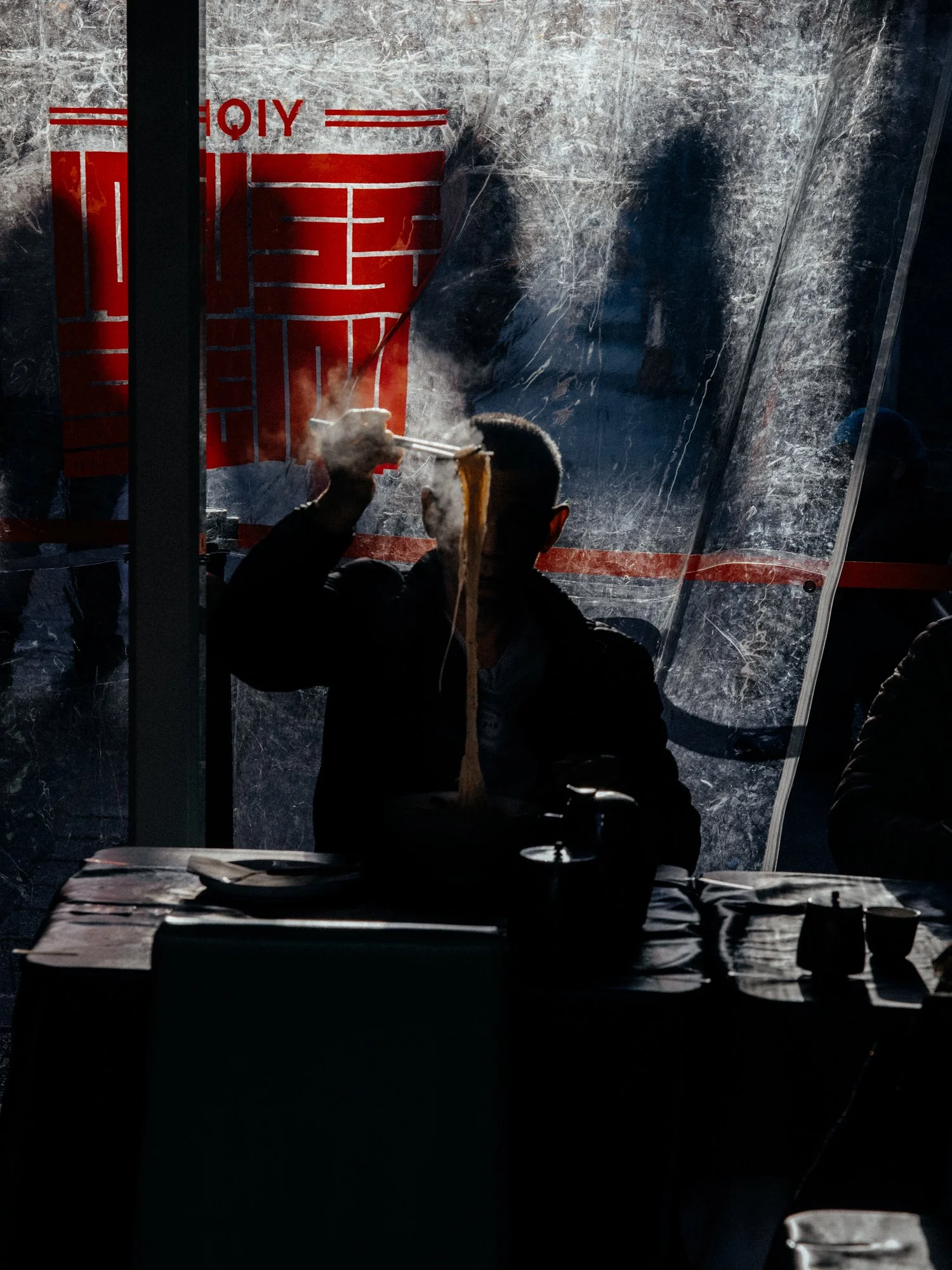 A lone human silhouette having noodles in London Chinatown. High contrast with vivid red on plastic by Joshua K Jackson.