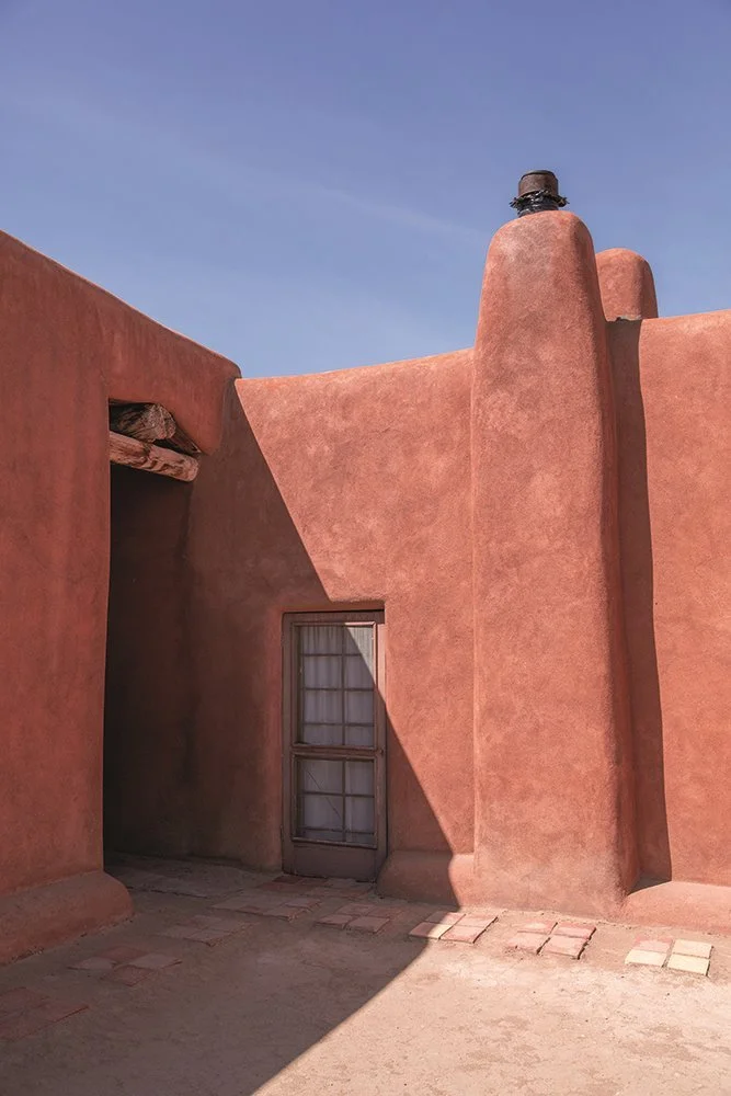 Edificio de adobe con puerta y ventana pequeñas, cielo despejado en el fondo.