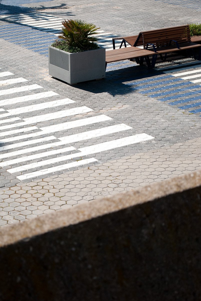 Cruce peatonal en pavimento adoquinado con banco y maceta grande con plantas. Fotografía digital de Barcelona. Fotografía urbana de Barcelona por Agosto Creative Studio.
