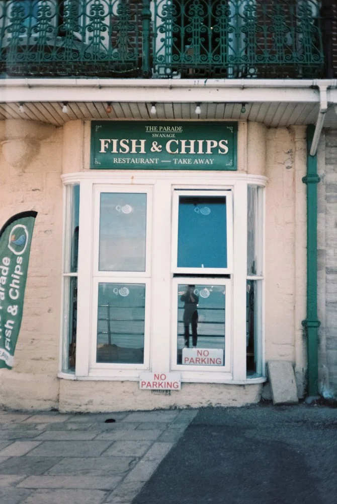 Cartel de un restaurante llamado 'Fish & Chips', que dice 'The Parade Swanage' y 'Restaurante - Take Away'.