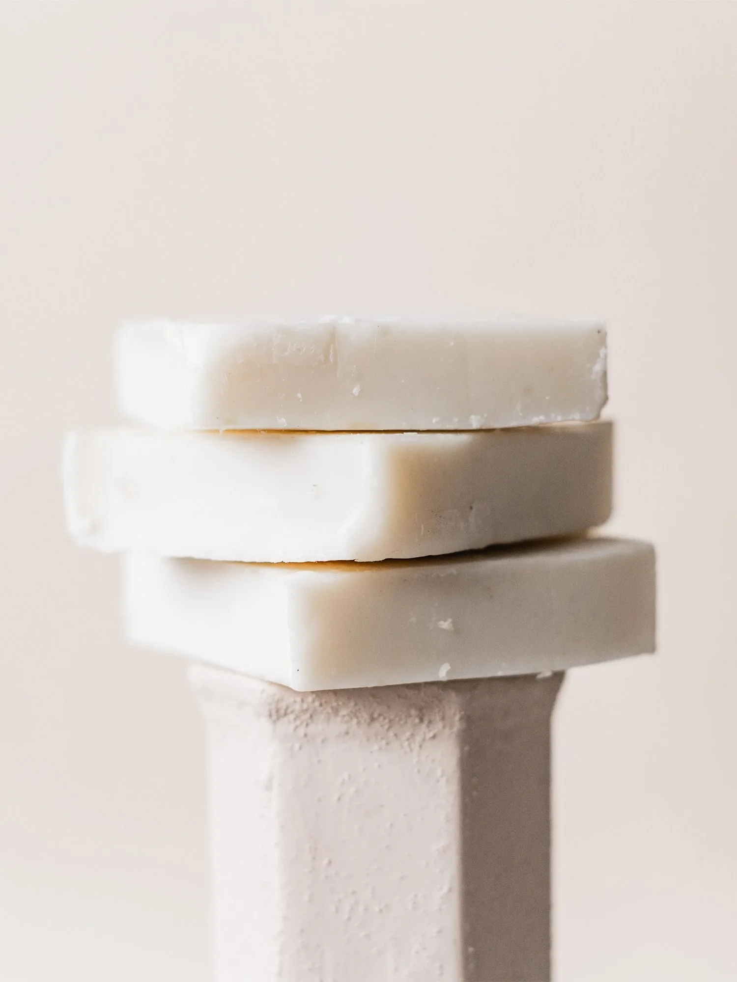 Tres barras de jabón apiladas en un pedestal beige con fondo neutro. Branding por Agosto Creative Studio. Branding y diseño de identidad visual y logotipo de marca de skincare y jabones.