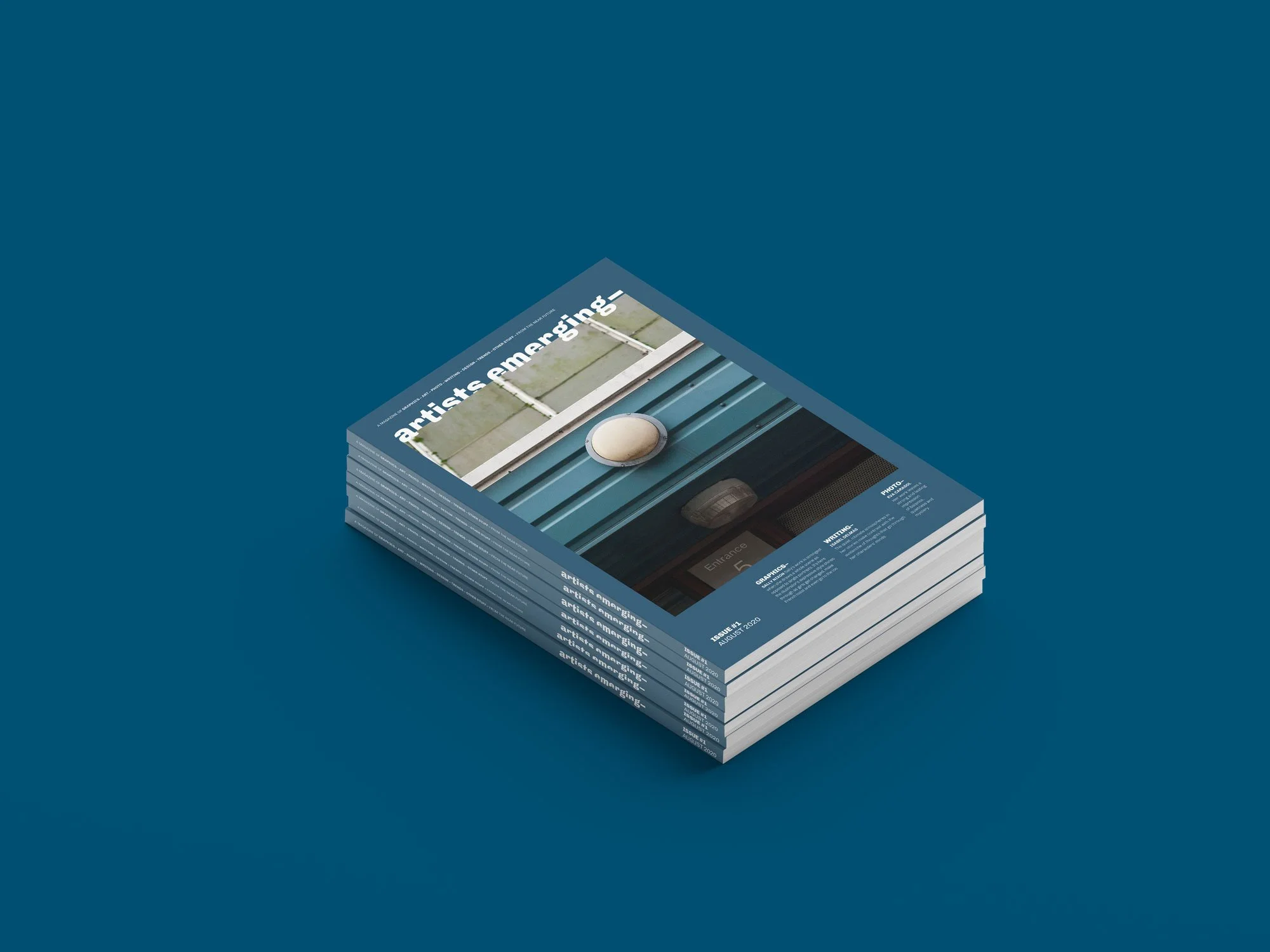 Revistas apiladas sobre un fondo azul con la portada que dice "artists emerging" y una imagen de una estructura arquitectónica. Diseño editorial. Editorial design. Agosto Creative Studio.