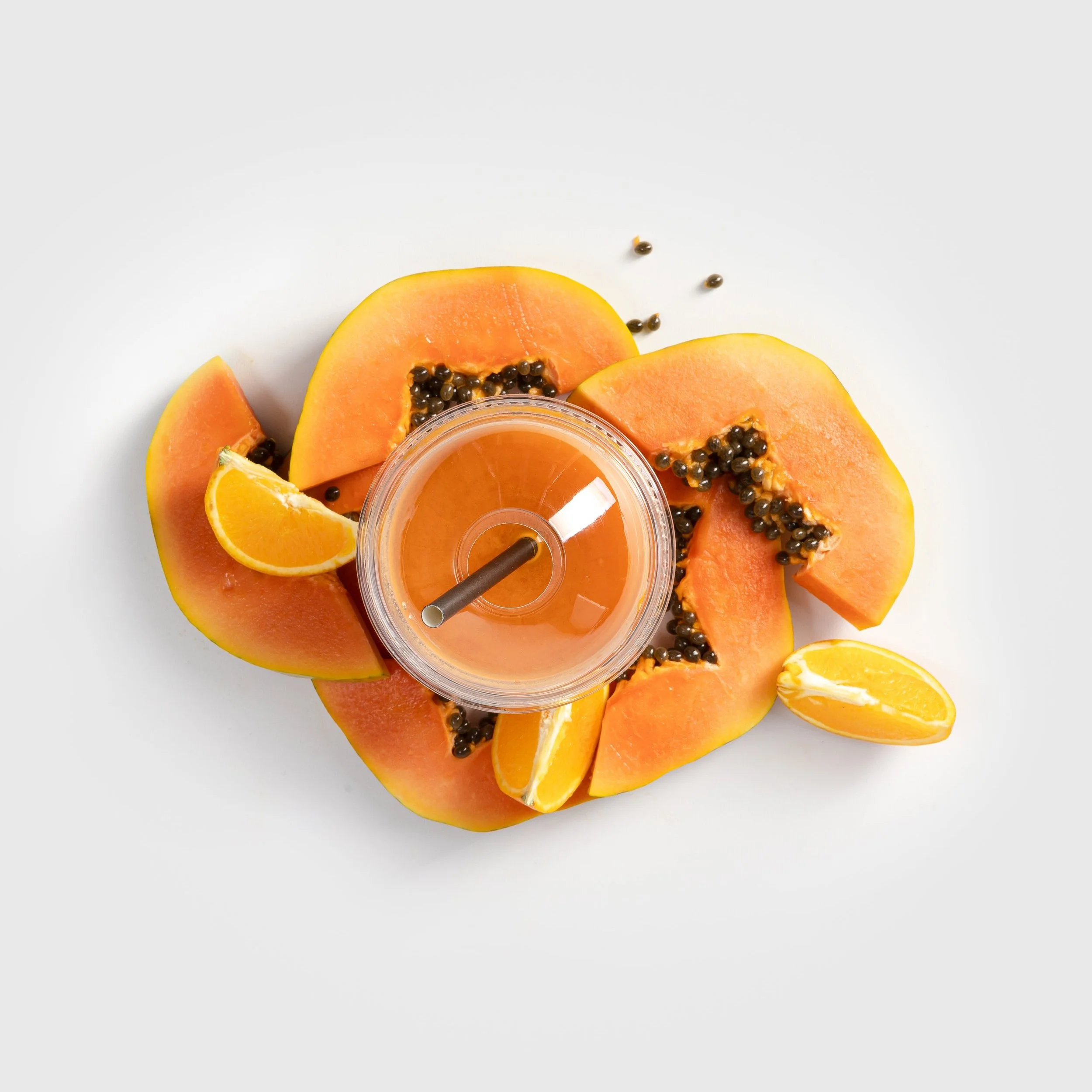 Vasos de jugo de naranja con rodajas de naranja y papaya en un fondo blanco.