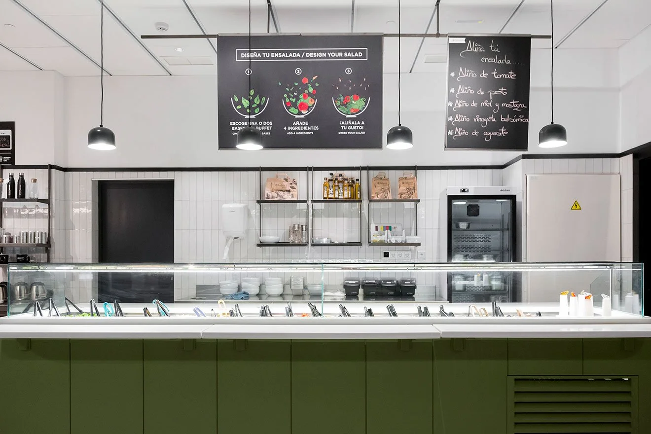 Mostrador de ensaladas en un restaurante con instrucciones para personalizar ensaladas y varios aderezos disponibles. Diseño de interiorismo comercial. Retail design. Diseño de bares y restaurantes. Foto de Eva Carasol.