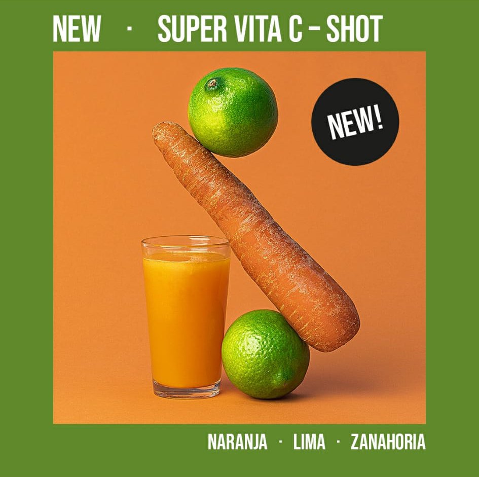 Imagen de un vaso de jugo de color naranja, acompañado por una zanahoria, una lima y un limón, con un fondo naranja y borde verde. Texto sobre el producto "Super Vita C - Shot" destacando los ingredientes: naranja, lima y zanahoria. Etiqueta "NEW" se
