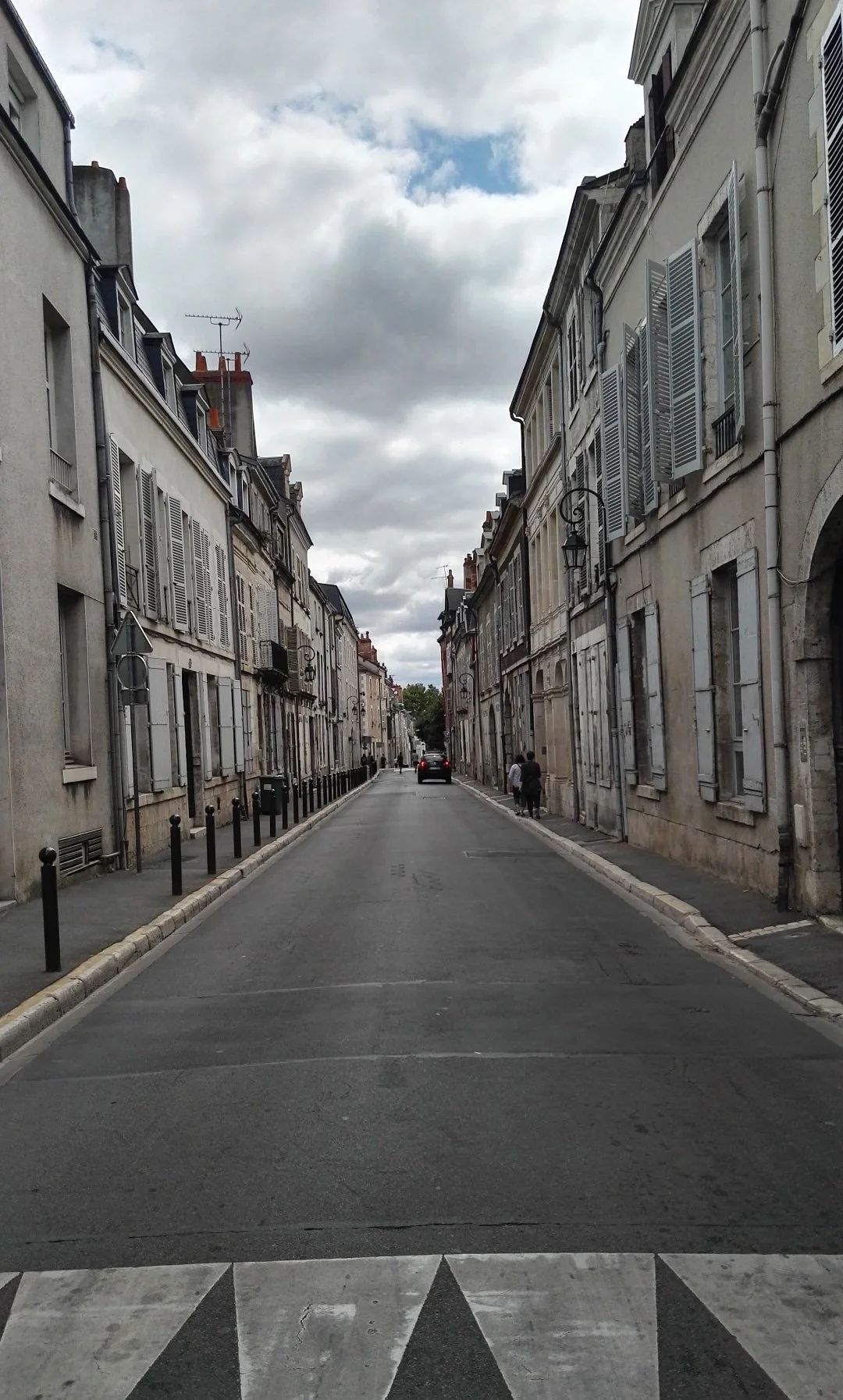 Calles de París con edificios de estilo clásico, cielo nublado, y una calle vacía con algunos peatones a la distancia.