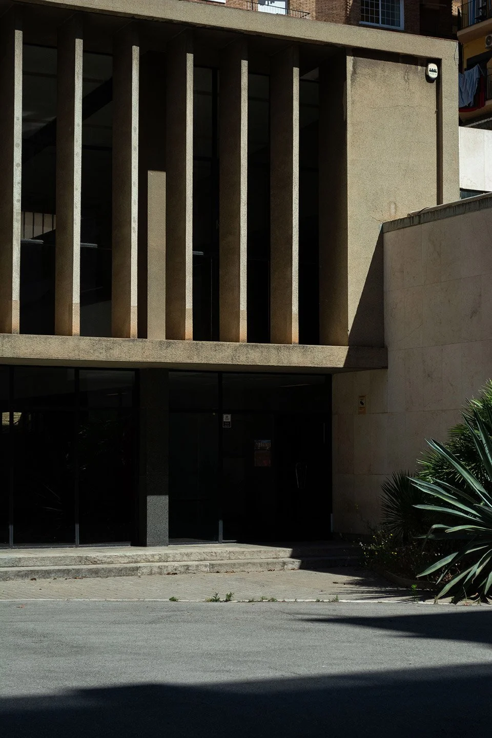 Fachada de un edificio moderno de concreto con columnas verticales y entrada de vidrio y metal en la planta baja