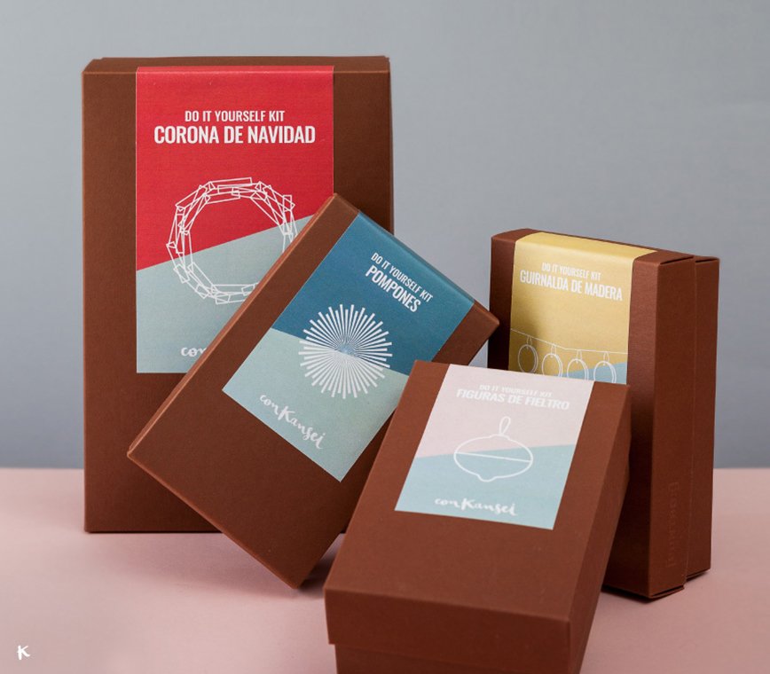 Kits de bricolaje para Navidad con etiquetas que dicen 'Corona de Navidad', 'Pompones', 'Guirnalda de madera' y 'Figuras de fieltro', sobre cajas de papel marrón.