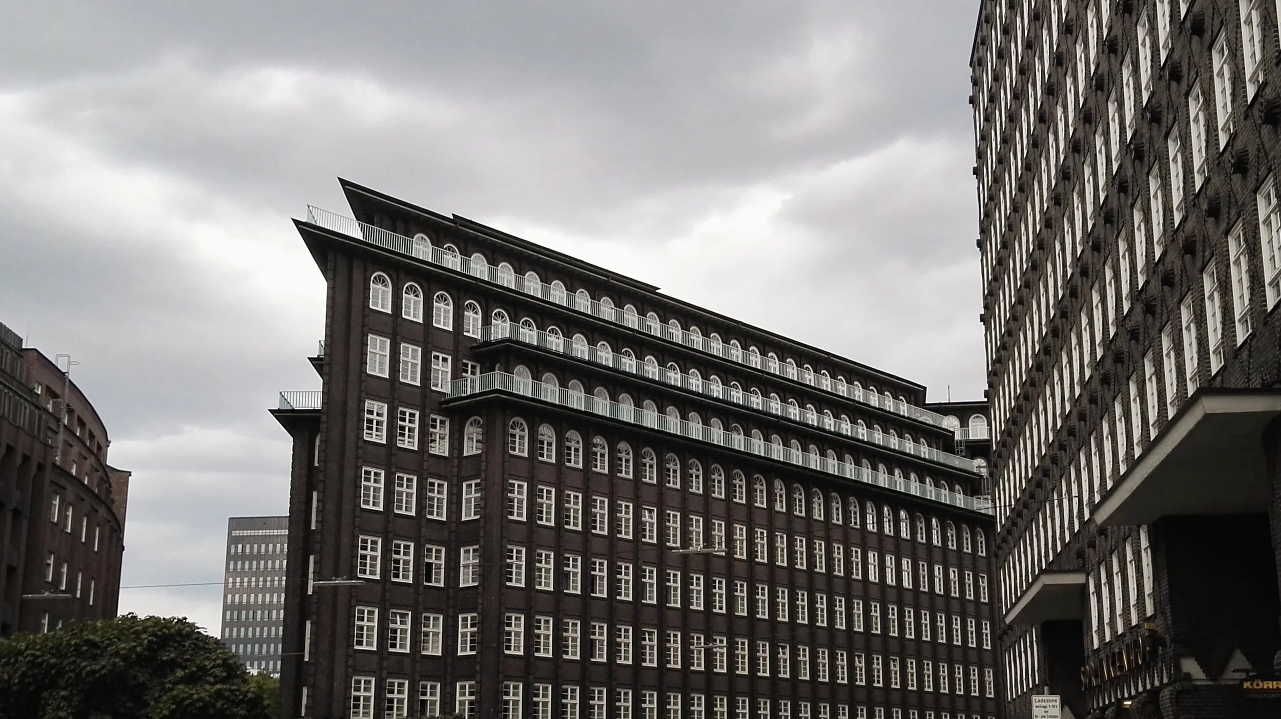 Edificio de color oscuro con muchas ventanas blancas y balcones en un día nublado en una ciudad. Hamburg.