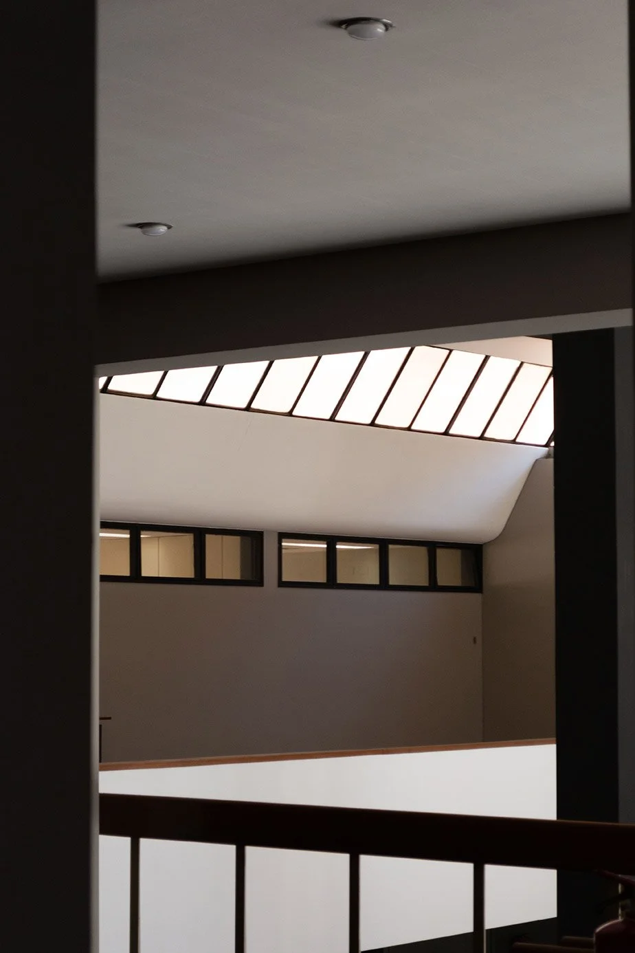 Vista desde una rampa que se dirige a un techo con ventanales rectangulares y una claraboya en forma de semicírculo en un interior moderno y minimalista.