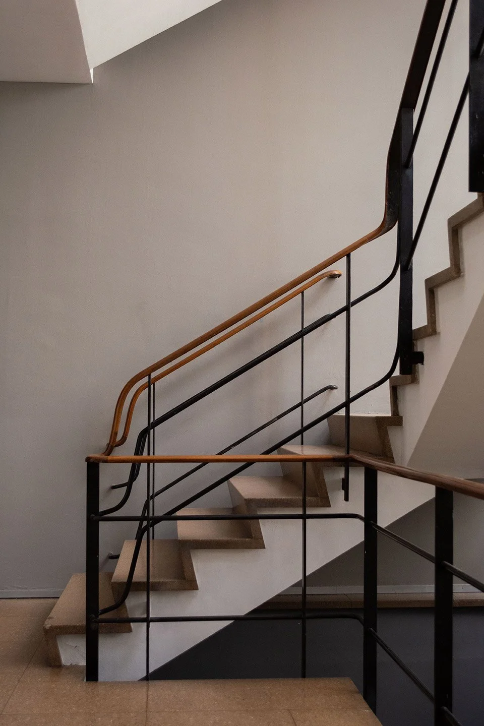 Escalera interna con barandilla de madera y barras de metal en una pared blanca.