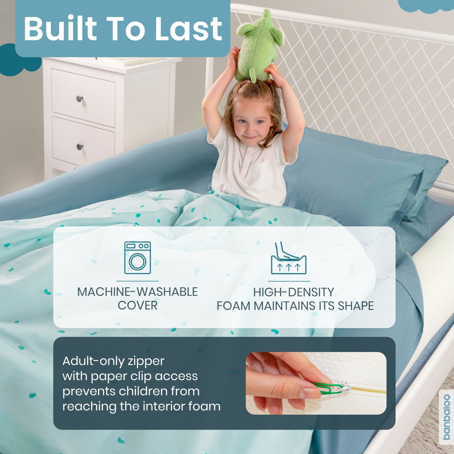 Una niña en la cama sosteniendo un peluche verde sobre su cabeza. La imagen muestra un edredón de color azul y la cabecera de la cama, con etiquetas sobre las características del producto. Incluye un icono de lavadora y texto que dice 'Funda lavable 