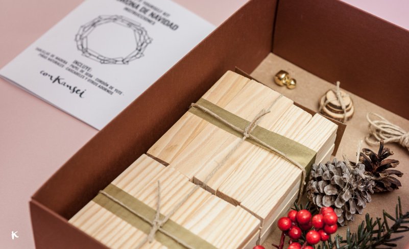 Caja de regalos de madera con decoraciones navideñas como piñas, almendras cubiertas de oro, piñas, ramas de pino, y frutos rojos.