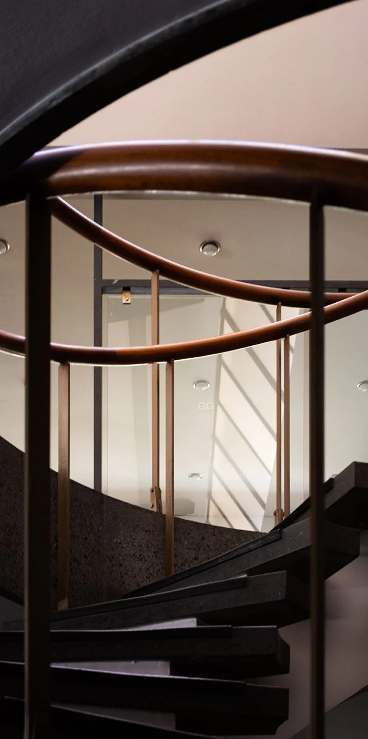 Escalera de caracol con barandales de madera y pasamanos de metal, vista desde abajo hacia arriba.