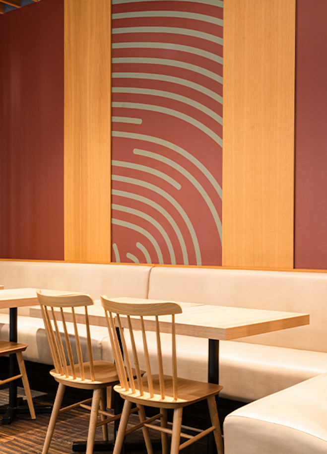 Área de comedor con paredes de madera, sillas de madera, mesa de madera y un tapiz decorativo en la pared con patrón de laberinto en color rosa y beige.