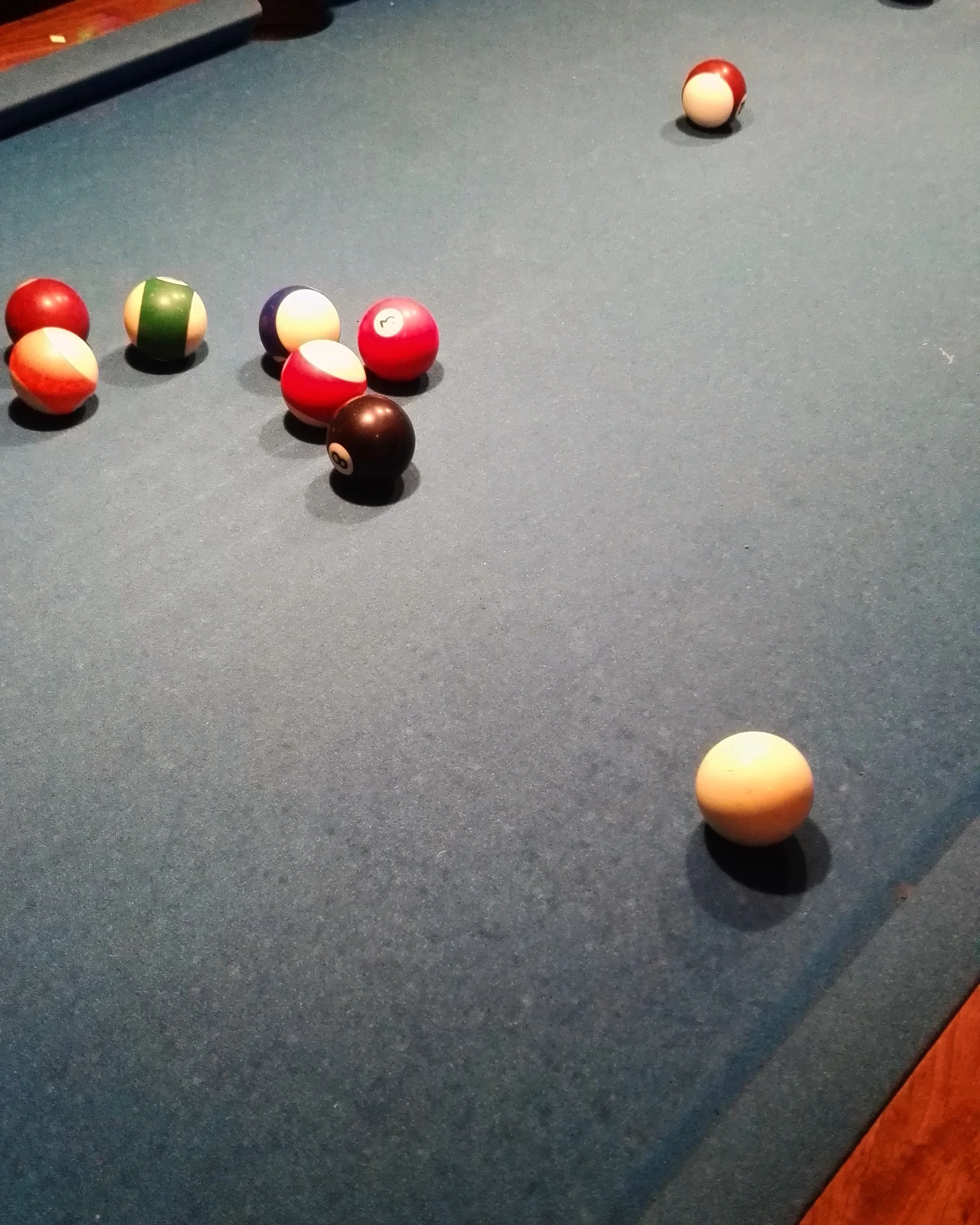 Mesa de billar con bolas dispersas, incluyendo la bola 8 y la bola blanca de golpe, en un juego de billar.