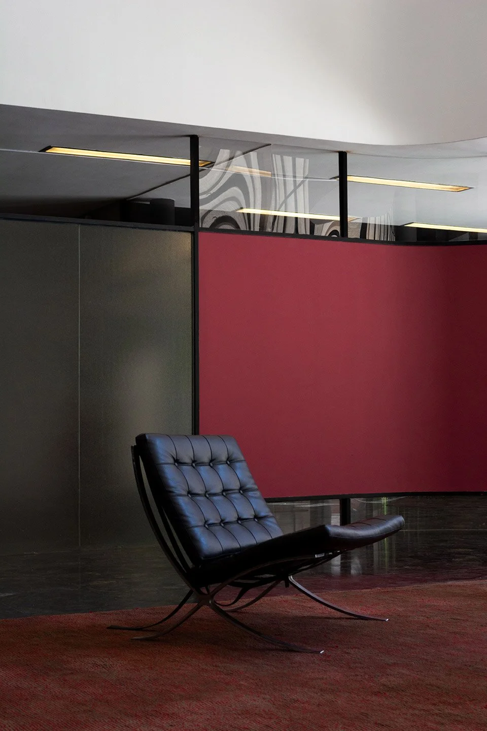 Sillón de diseño moderno negro en un espacio interior, con pared roja y paredes de vidrio.