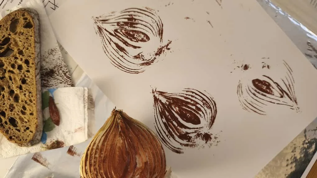 Un papel con impresiones de cebollas, una cebolla, y una rebanada de pan en una superficie de trabajo. Agosto Creative Studio, diseño de tiendas y restaurantes. Retail Design. Branding. Fotografía.