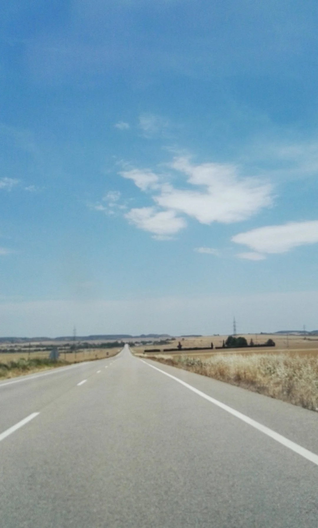 Camino desolado en un paisaje de campo con cielo despejado y algunas nubes, sin niños ni autos, en un día soleado y caluroso.