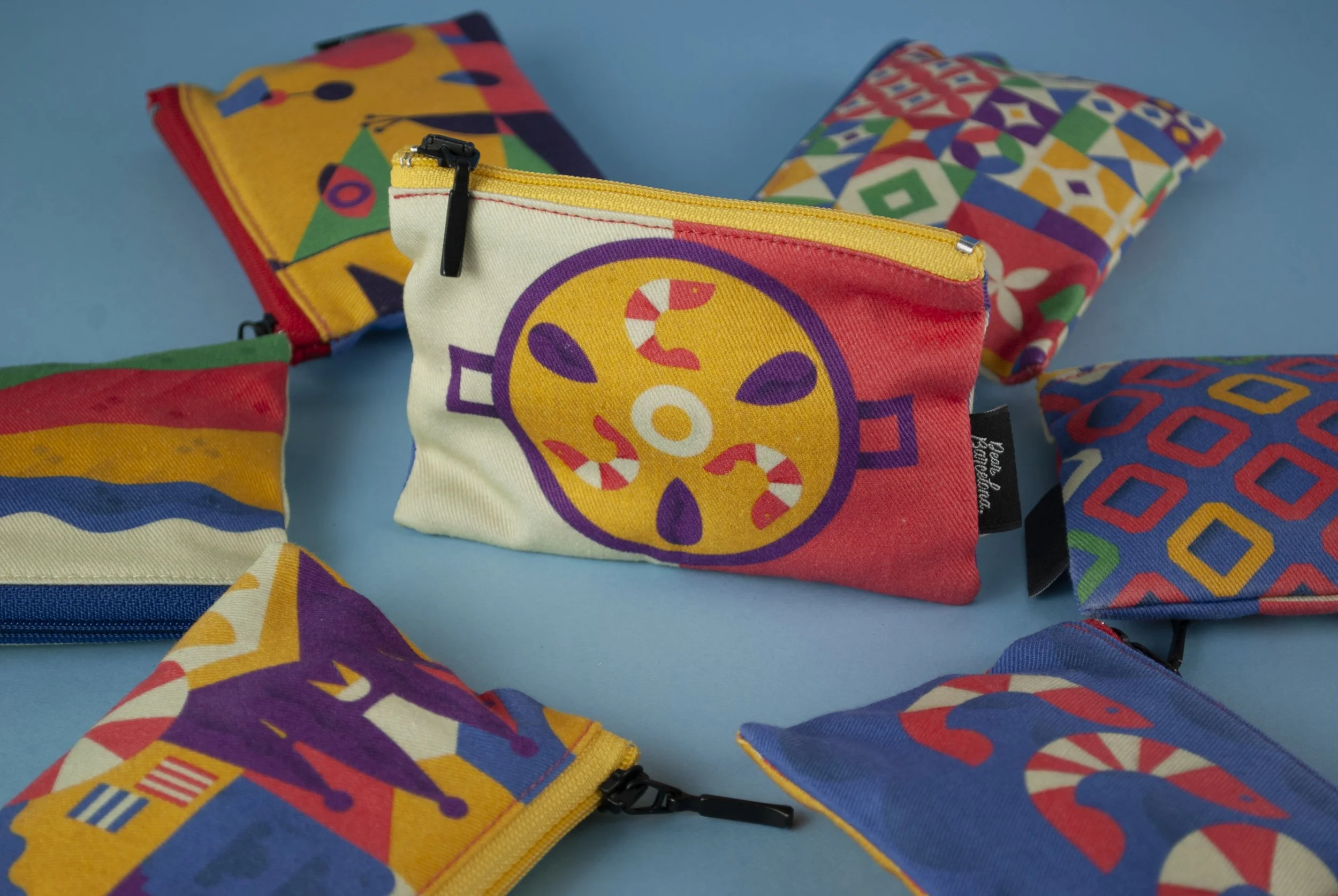 Varios monederos y bolsas pequeñas de tela con patrones coloridos, algunos con bordes de cremallera, sobre un fondo azul.