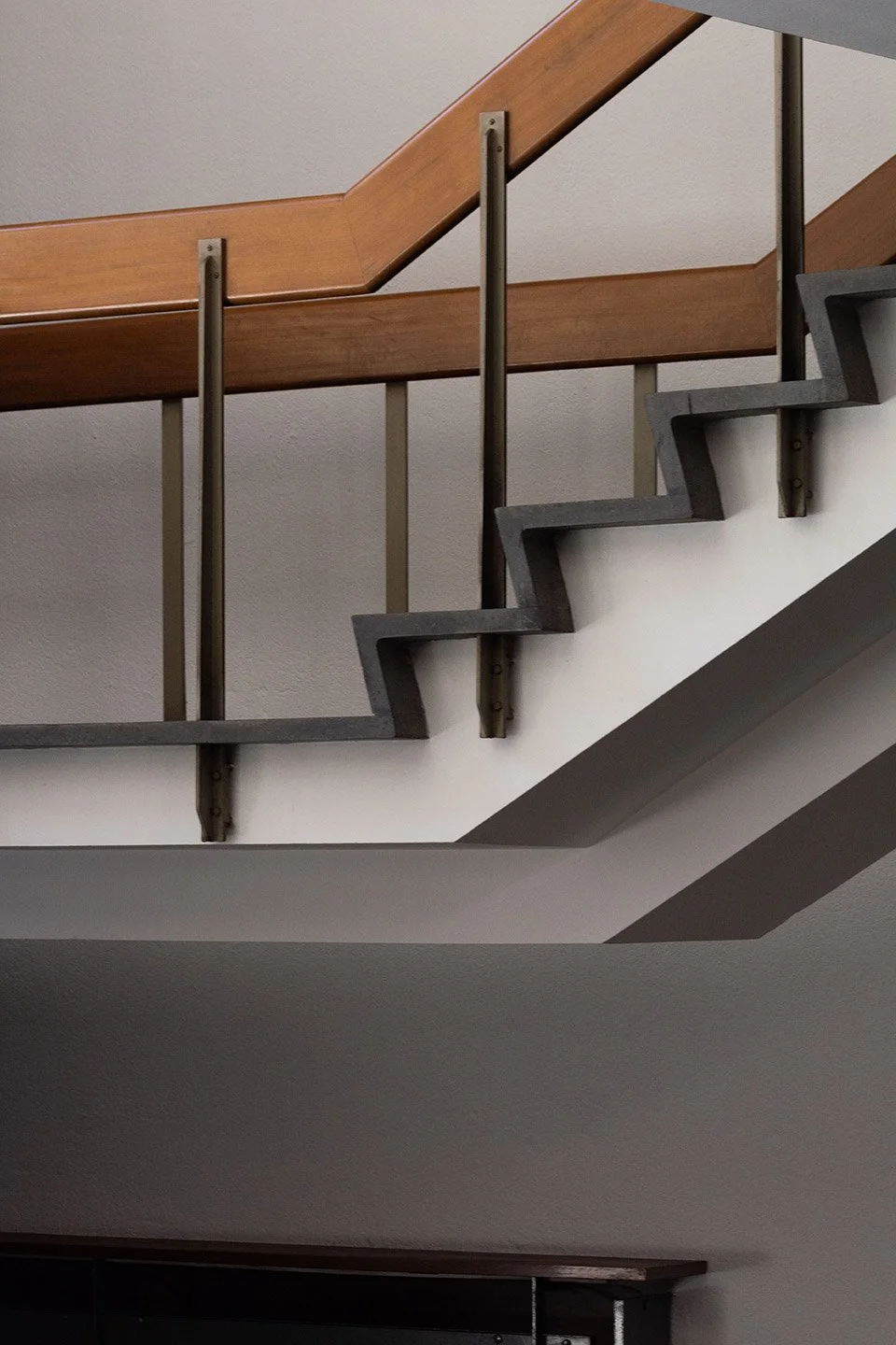 Escalera de interior con barandilla de madera y estructura de metal en una pared blanca.