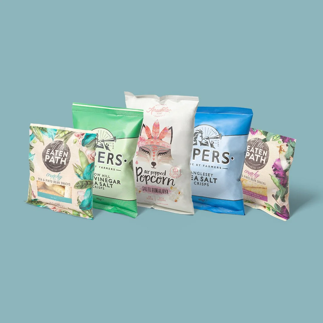 Varias bolsas de snacks, incluyendo palomitas, patatas fritas, y otros bocadillos en empaques coloridos con diseños florales y de animales.