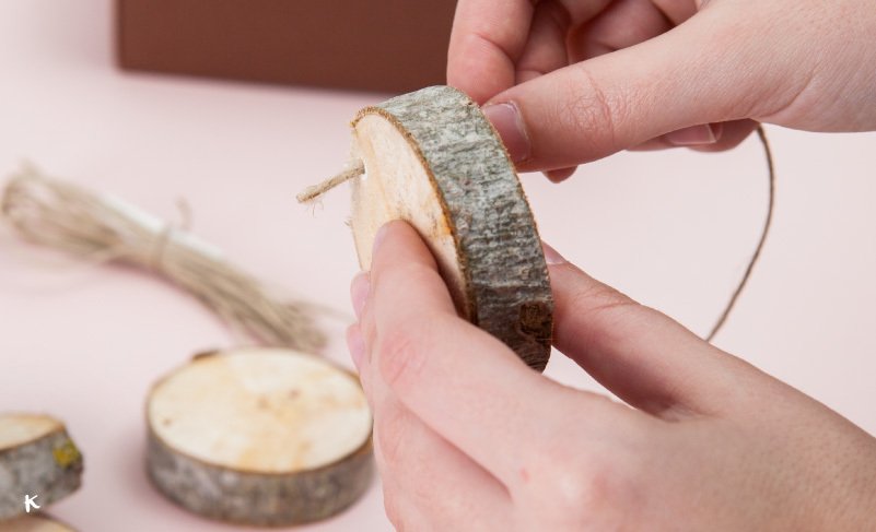 Persona creando una decoración con rodajas de madera y cuerda.