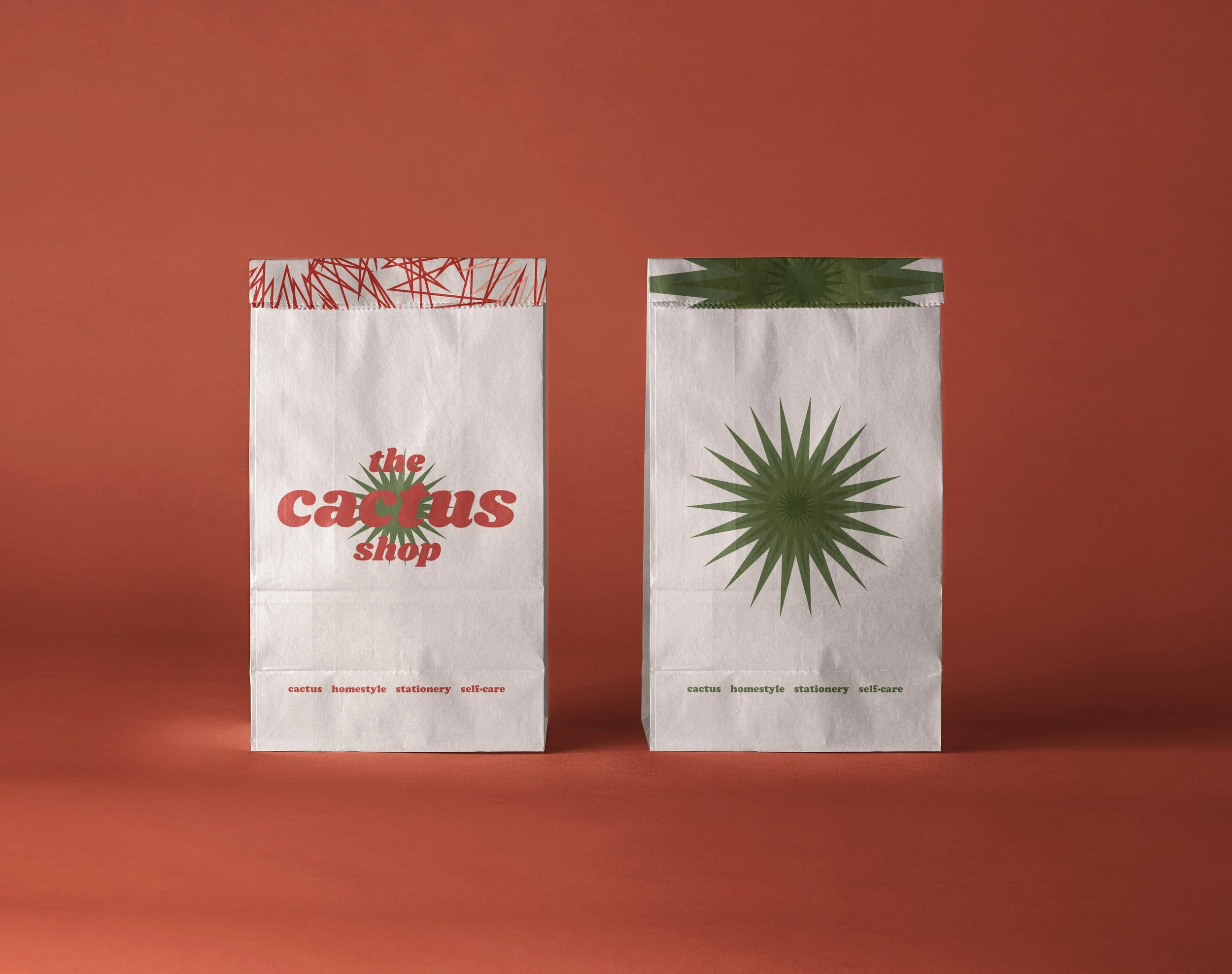 Dos bolsas de papel con diseños de cactus, una con la inscripción "the cactus shop", en un fondo rojo. The Cactus Shop, diseño gráfico, branding y packaging. Agosto Creative Studio.