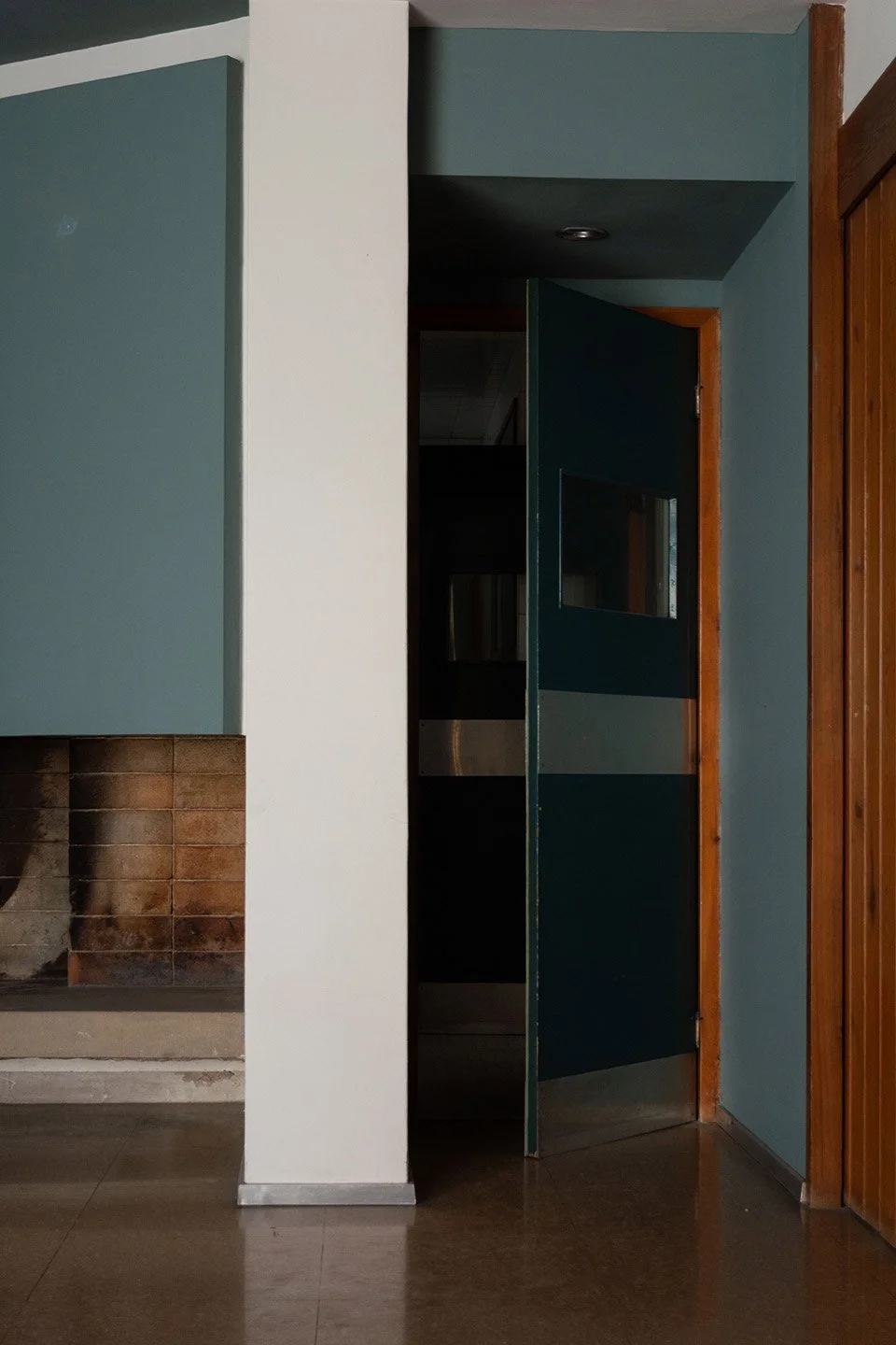 Imagen de una habitación con una chimenea, una pared blanca, una puerta azul y paredes de madera.