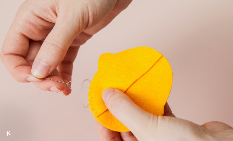 Una mano cose una pieza de fieltro amarillo en forma de corazón con una aguja e hilo.