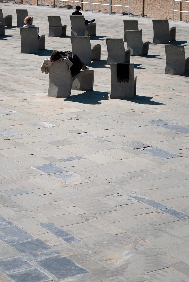 Varias personas sentadas en sillas de cemento en una plaza al aire libre. Fotografía digital de Barcelona. Fotografía urbana de Barcelona por Agosto Creative Studio.