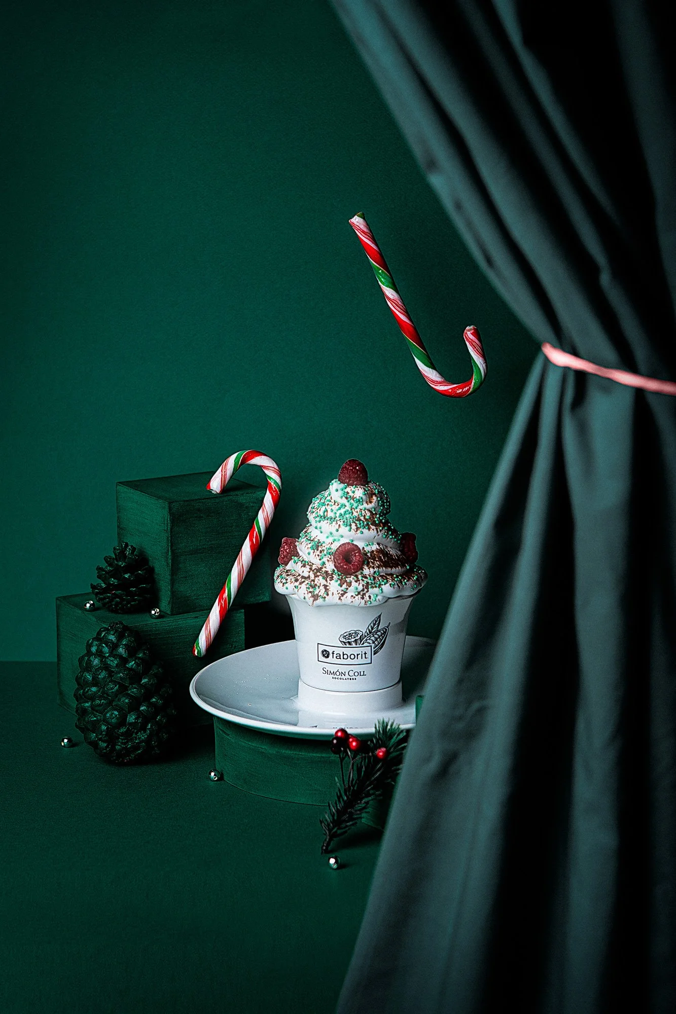 Postre navideño con helado, decorado con cerezas, glucosa, y confites, rodeado de piñas y adornos de Navidad, con caramelos en forma de bastón en el fondo.