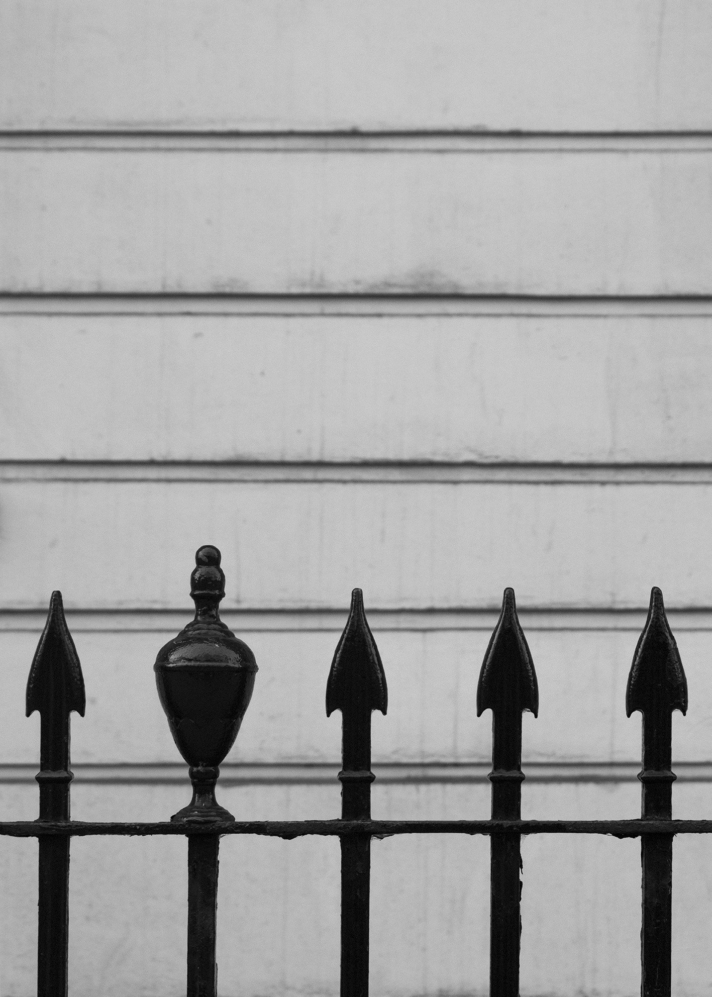 Reja de hierro negro con diseño decorativo frente a pared blanca con líneas horizontales. Fotografía arquitectónica de Londres. London architecture photography. Por Agosto Creative Studio Barcelona. Agencia de diseño y comunicación Barcelona.