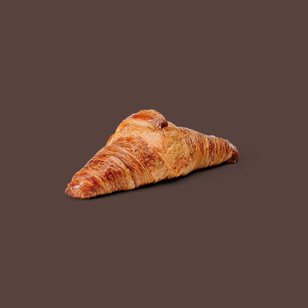 Un croissant de mantequilla horneado sobre un fondo marrón.