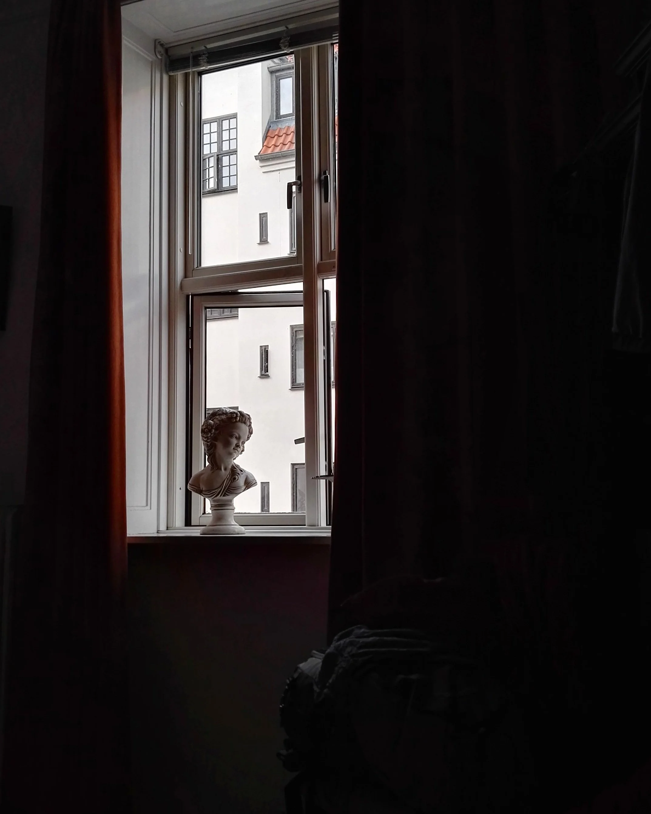 Escultura de busto de una mujer en una ventana en una habitación oscura.