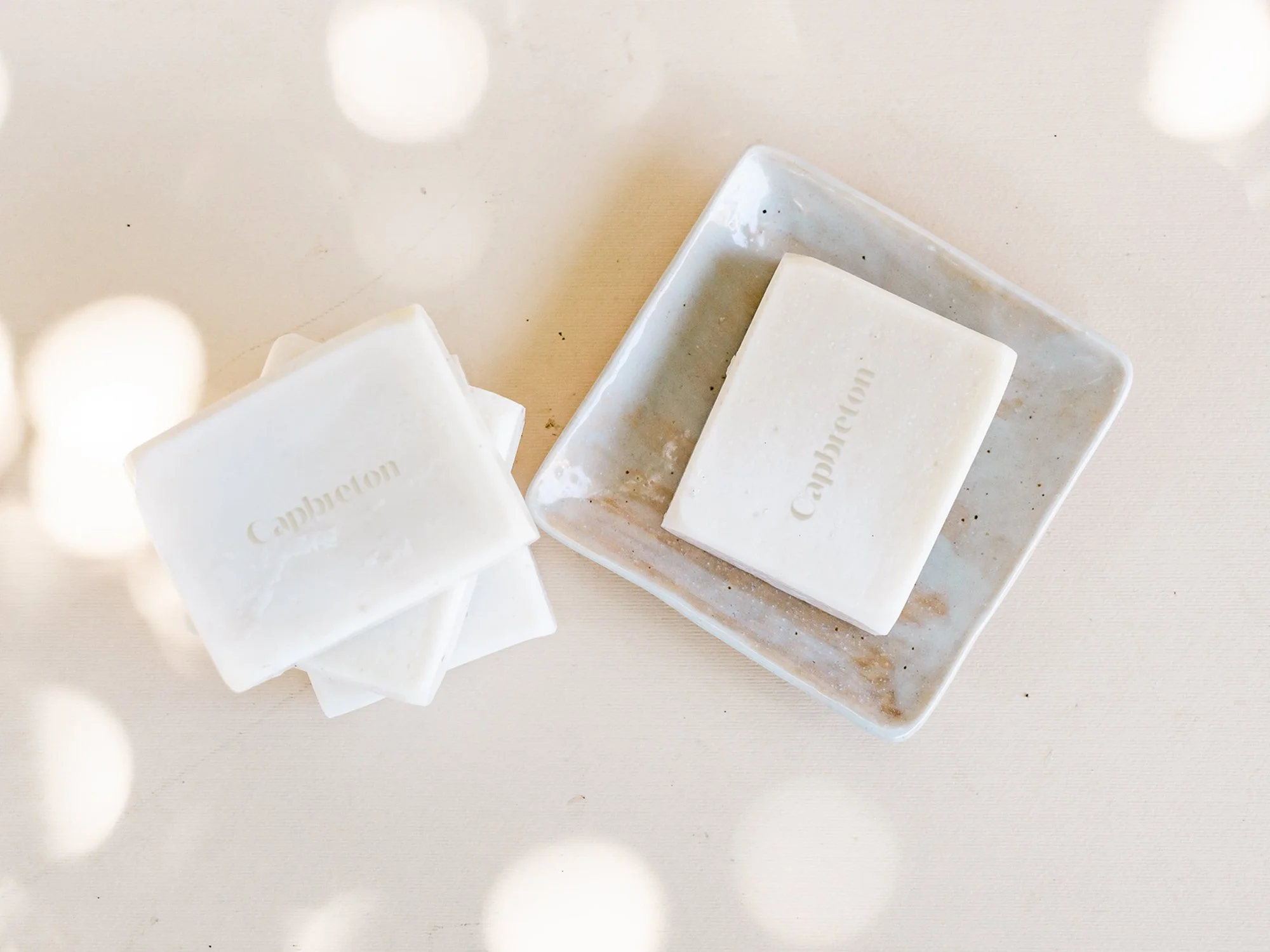 Barras de jabón Capbreton sobre un platillo rectangular en una superficie clara con luces circulares. Branding por Agosto Creative Studio. Branding y diseño de identidad visual y logotipo de marca de skincare y jabones.