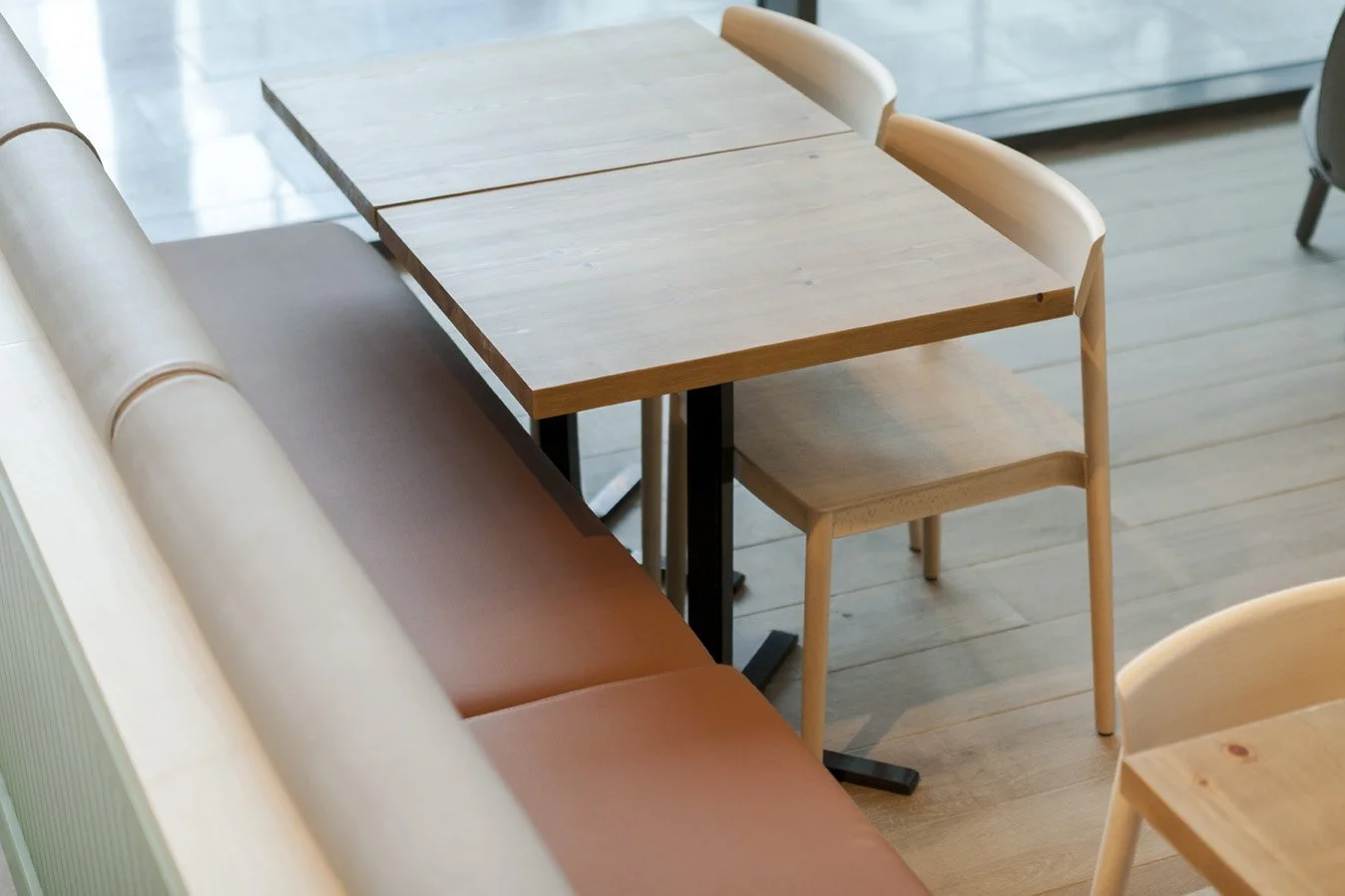 Muebles de una cafetería vacía, con una mesa de madera clara, una banca acolchada y sillas de madera.