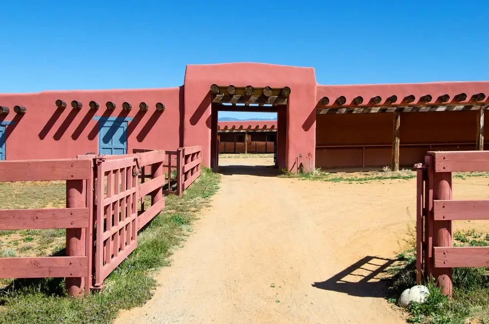 Entrada a rancho con arquitectura de estilo adobe, puertas de madera y un camino de tierra.