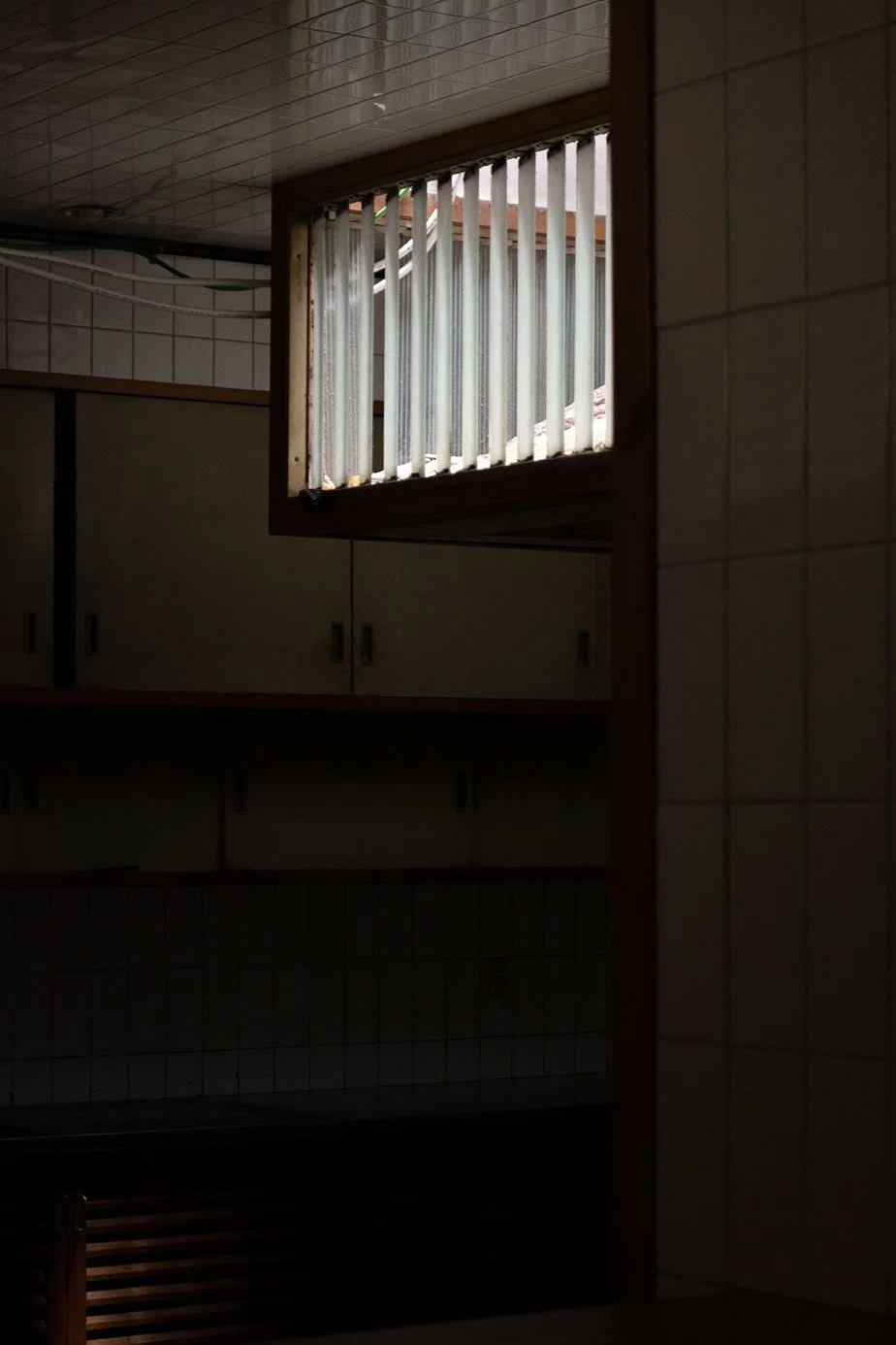 Ventana con barrotes en una pared de azulejos beige en un espacio interior oscuro.