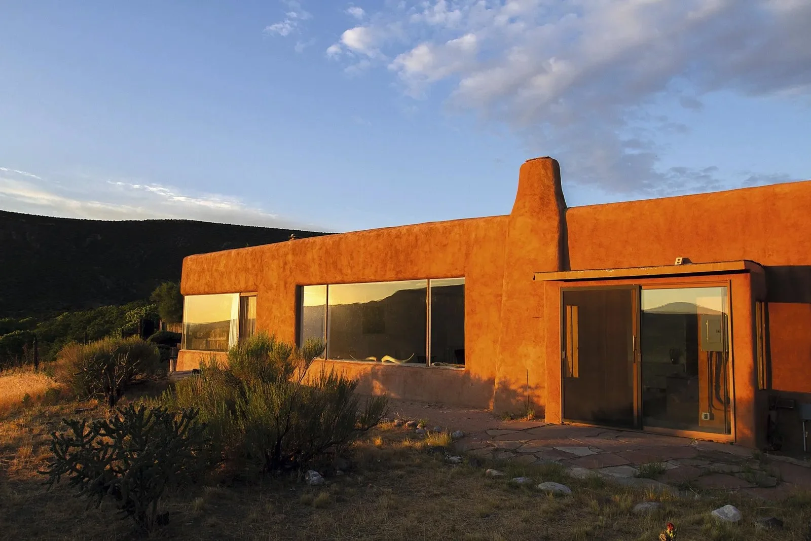 Casa de adobe en un paisaje desértico con plantas y un cielo azul.