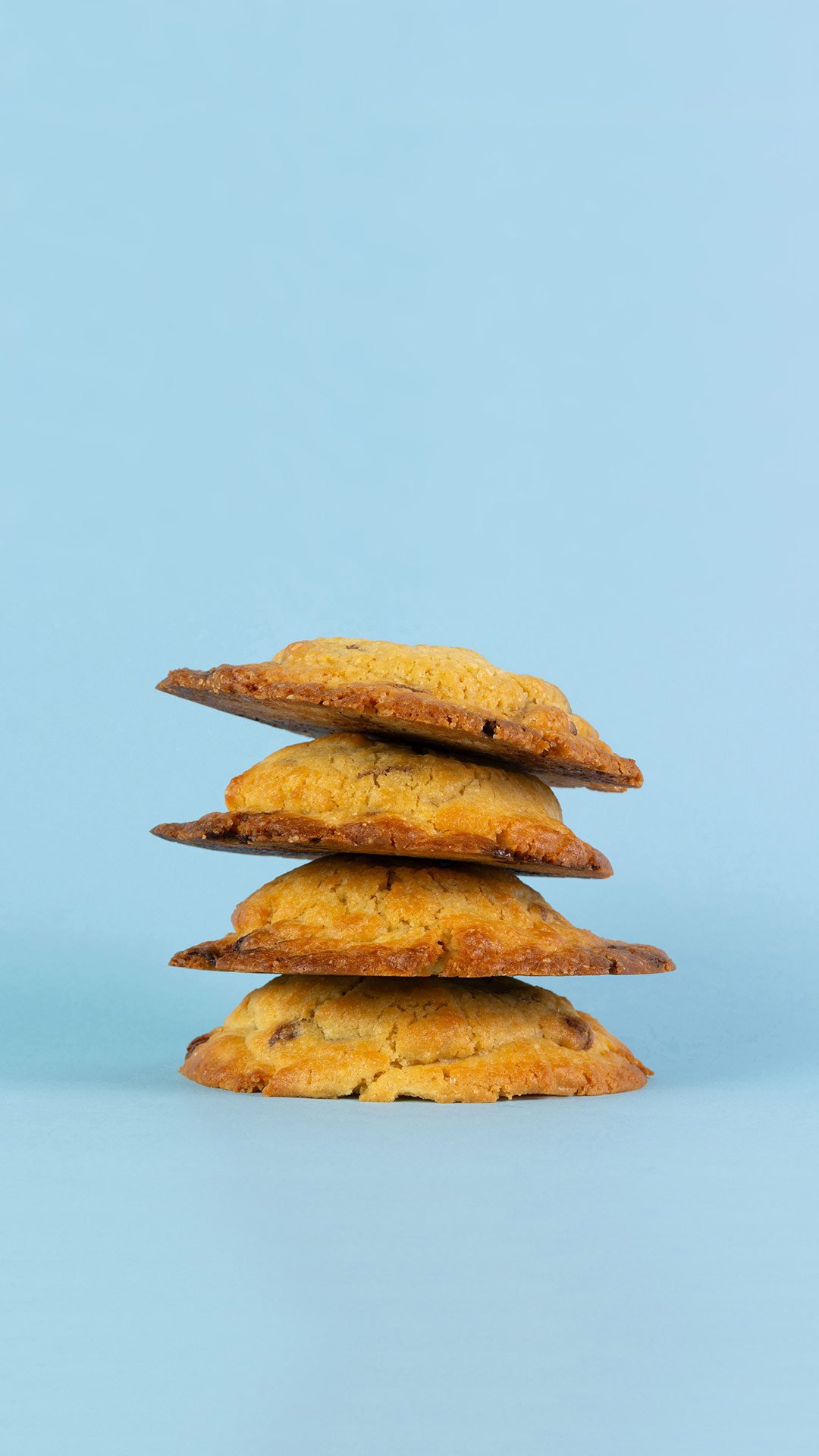 Cuatro galletas apiladas, de diferentes tonos dorados, sobre un fondo azul claro. Mionas Bakery. Especialidad en Cookies en Sitges. Retail Design, diseño de tiendas. Foto de producto.