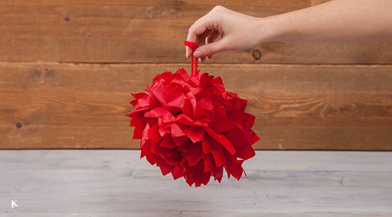 Mano sosteniendo una piñata de papel en forma de bola de color rojo.