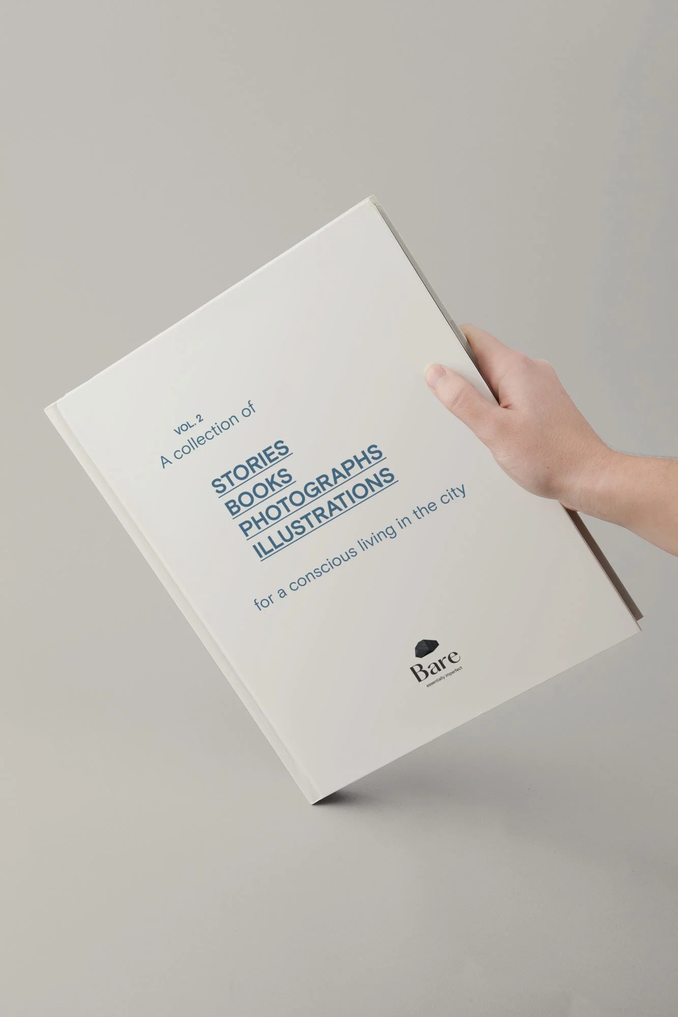 Mano sosteniendo un libro titulado "A collection of STORIES BOOKS PHOTOGRAPHS ILLUSTRATIONS" de Bare. Por Agosto Creative Studio Barcelona. Agencia de diseño y comunicación Barcelona.